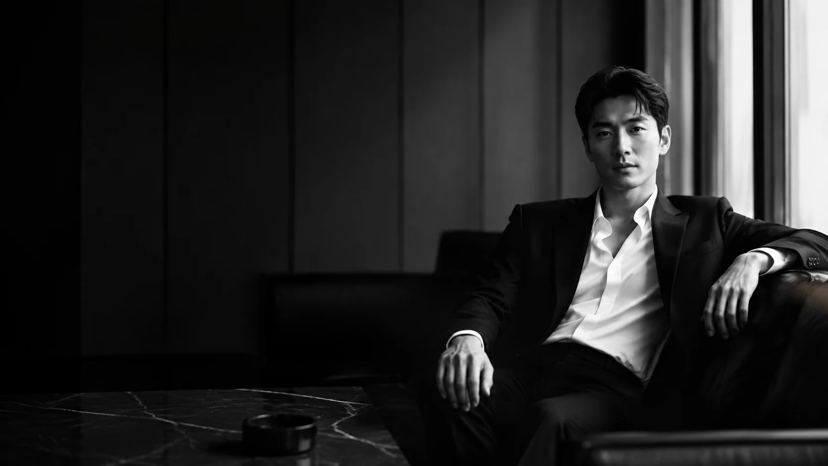 강남호빠 콘셉트 화보 — 어두운 라운지 소파에 앉은 블랙 수트 차림의 성인 남성
